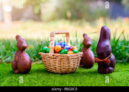 Chocolate Easter bunny with straw basket full of colourful eggs on green grass background Stock Photo