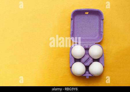 Easter composition. Set of Four white eggs in purple box on  yellow background Stock Photo