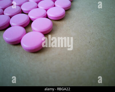 pink pills laid out in shape of a heart on brown background. coloured drugs. concept - heart disease, heart disorders and drugs, cardiology, valentine Stock Photo