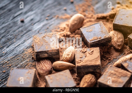 Pieces of dark bitter chocolate with cocoa powder and almonds nuts on wooden background. Card with space for text Stock Photo