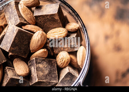 Pieces of dark bitter chocolate with cocoa powder and nuts almonds on wooden background. The concept of confectionery ingredients Stock Photo