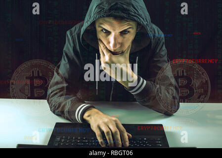 A hacker with a face is trying to steal cryptocurrency using a computer. Scam at Cryptojacking Stock Photo
