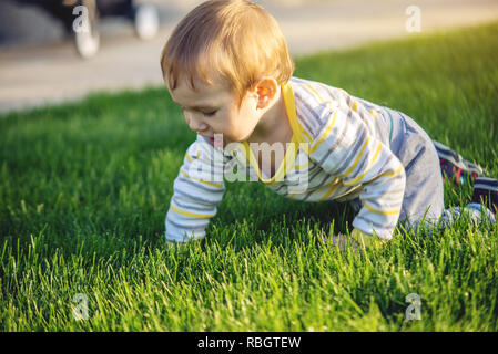 Cute baby sits on a green lawn in nature on a Sunny autumn day. The concept one-year-old child Stock Photo