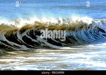 Large waves form off of the coast of long island on a stormy day with a surfer in the background. Stock Photo