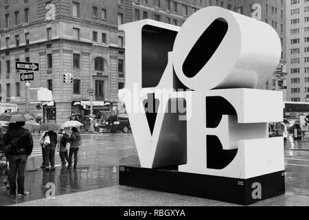NEW YORK, USA - JUNE 7, 2013: People walk past Love sculpture in rain in New York City. The famous monument by Robert Indiana is located on 6th Avenue Stock Photo