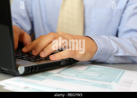 Man in blue shirt and tie works, sitting at a table with laptop. Male hands typing on keyboard, concept of office manager, staffing, completing the ta Stock Photo