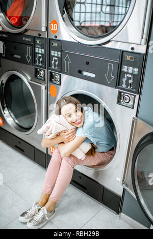 Portrait of a cheerful woman with clean and fresh towels sitting on the dryer machine in the laundry Stock Photo