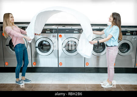 Young women throwing up a bedsheet making clothes after the washing in the public laundry Stock Photo