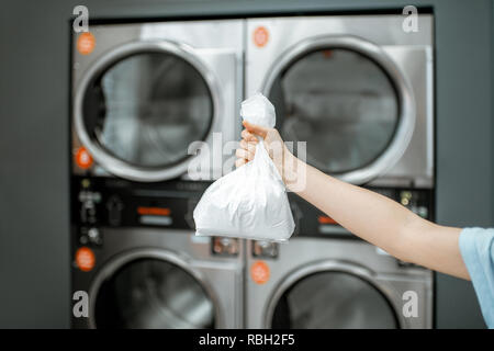Holding bag with white washing powder with professional machines on the background at the laundry