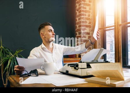 Young writer wearing glasses and white shirt sitting near the typewriter and considering new chapter of his book in the his office Stock Photo