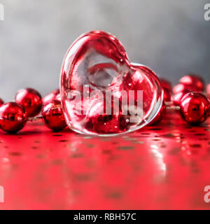Shining transparent heart and a group of red beads. Perfect Valentine's Day greeting card background. Image in red tone on grey background in a 1x1 Stock Photo