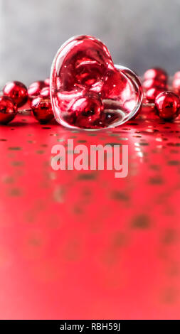 Shining transparent heart and a group of red beads. Perfect Valentine's Day greeting card background. Vertical image in red tone on grey background Stock Photo