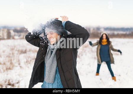 Snowball fight. Winter couple having fun playing in snow outdoors. Young joyful happy young man and woman. Stock Photo