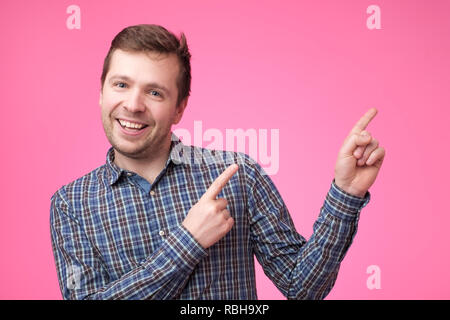 Happy beautiful bearded guy looking at camera, smiling and pointing aside with hand. Stock Photo