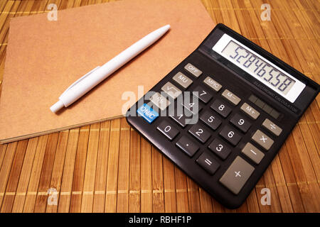 Classic electronic calculator displaying random numbers with a notebook and a white pen on a wood table Stock Photo