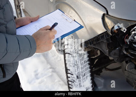 Insurance agent checking car after car accident and filling accident details form. Winter time. Focus on hands. Stock Photo
