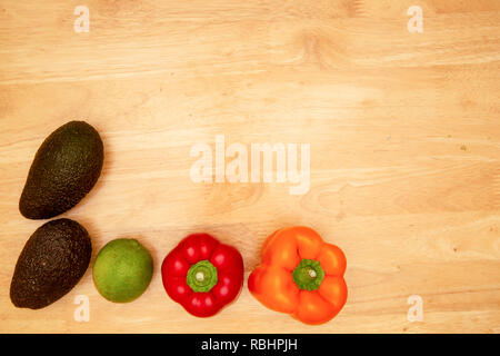 Colorful vegetables: Two peppers, one lime and two avocados sitting on a kitchen table. Stock Photo