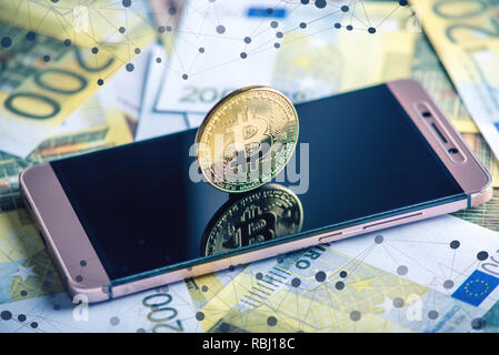Bitcoin coin on the phone screen on the background of the Euro banknotes. The blockchain and the future of cryptocurrency Stock Photo