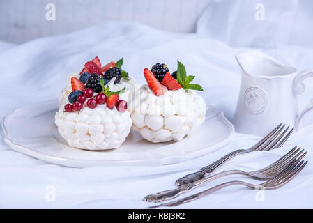 Delicate white meringues with fresh berries on the plate. Dessert Pavlova. White background. A festive wedding cake. Stock Photo