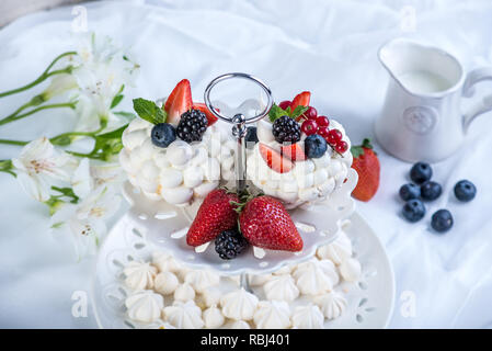 Delicate white meringues with fresh berries on the plate. Dessert Pavlova. White background. A festive wedding cake. Stock Photo