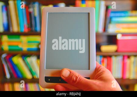 Ebook or digital reading tablet device. E-book in man's hand. On the background is the shelf with bright real books. Online shopping books concept Stock Photo