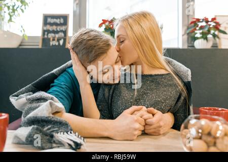 Kissing embracing young couple sitting in cafe together under one warm blanket. Stock Photo