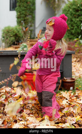 A four year old girl laughing and playing in drifts of fallen autumn leaves in Quebec, Canada Stock Photo