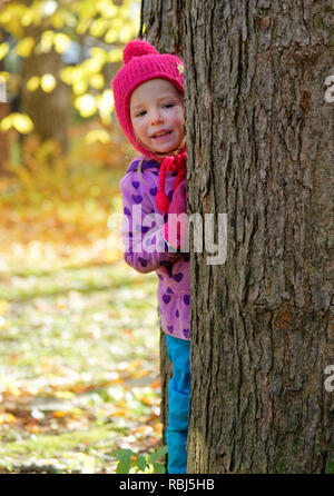 A little girl (4 yrs old) looking out from between two trees Stock Photo