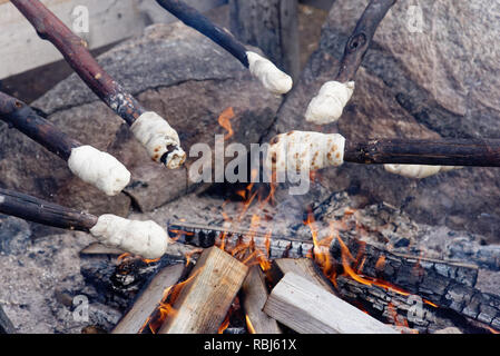 Cooking bannock campfire bread on sticks over an open fire Stock Photo