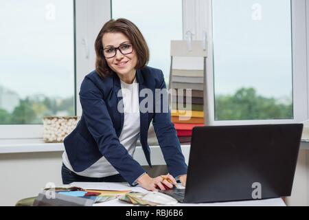 Designer or architect posing and looking at you works with samples of fabrics for curtains and blinds, background office window. Business - textile in Stock Photo