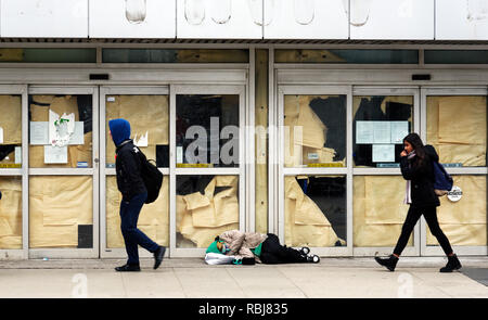 A homeless person sleeping on the pavement in front of a closed store as people walk by in Toronto, Canada Stock Photo