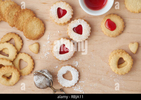 Top view of traditional Linzer cookies filled with strawberry jam on wooden board with heart-shaped openings. Valentine's day concept. Stock Photo