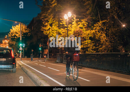 STRASBOURG, FRANCE - OCT 31, 2017: Senior woman riding a bike at night in central Strasbourg going home - wearing protection helmet  Stock Photo