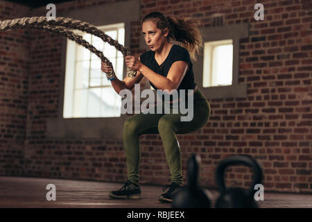 fitness woman using battle ropes for exercising. Female working out with battle ropes at cross training gym. Stock Photo