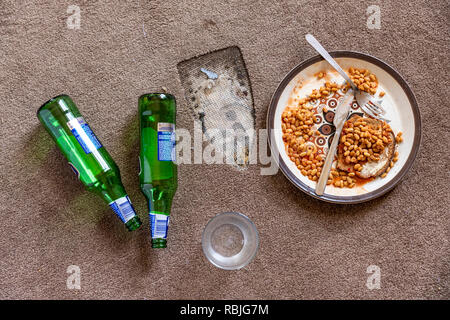 The floor of a student flat - congealed baked beans - iron burn mark on the carpet - empty glass - beer bottles Stock Photo
