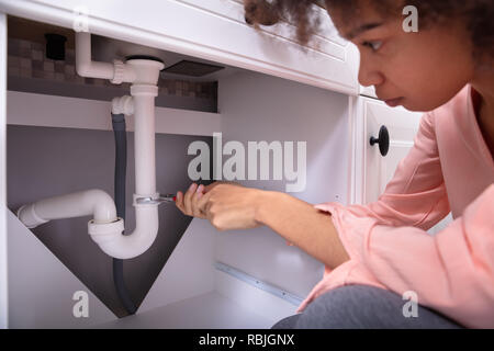 Close-up Of A Concentrated Young Woman Repairing White Sink Pipe With Adjustable Wrench Stock Photo