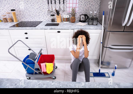 Exhausted African Young Woman Sitting On Floor In The Kitchen Stock Photo