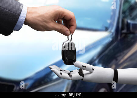 Close-up Of A Businessperson's Hand Giving Car Key To Robot Stock Photo