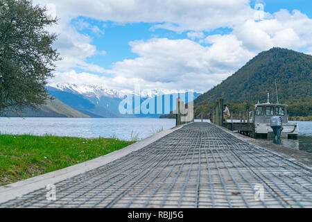 LAKE ROTOROA NEW ZEALAND - OCTOBER 6 2018; Two tourists on pier extending into scenic lake with boat moored alongside   surrounded by mountains of Nel Stock Photo