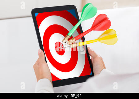 Human Hand Holding Digital Tablet With Colorful Darts On Target Over White Desk Stock Photo