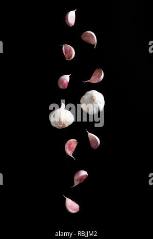 Falling Garlic bulbs and pink cloves of garlic isolated on black background Stock Photo