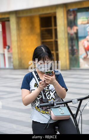 Female cyclist in Shanghai, China, wearing a face mask using her mobile phone Stock Photo