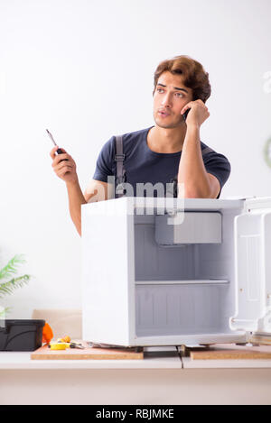 Young handsome contractor repairing fridge Stock Photo