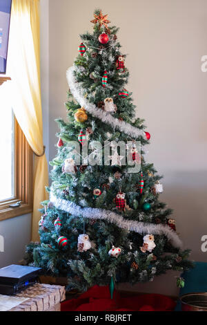 An artificial Christmas tree decorated with owl ornaments and balls standing in the corner of a home. USA Stock Photo