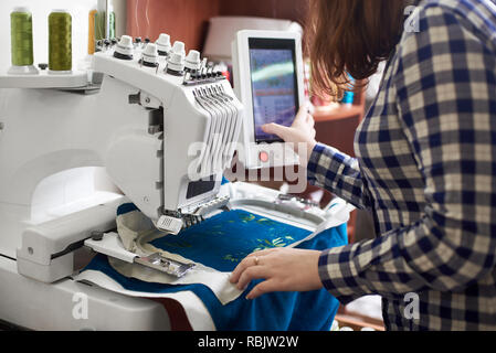 Close-up of woman working on modern computerized specially engineered embroidery machine with multi-needle fixed embroidery head creating green floral Stock Photo