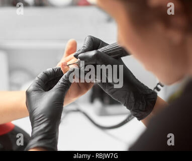 Process of manicure making in beauty salon. Close-up of professional master manicurist hands in black rubber gloves working on client fingernails with Stock Photo