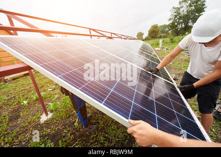 Team of workers assembling exterior stand-alone solar photo voltaic panel system on sunny summer day. Alternative renewable ecological green energy so Stock Photo