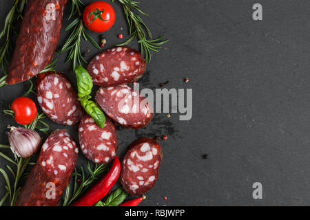 Smoked sliced salami on black slate background. Sausages with rosemary, basil, tomato and pepper. top view with copy space Stock Photo