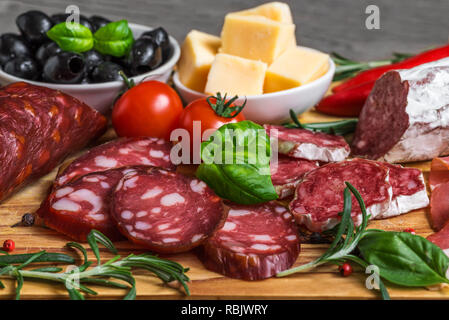 Food tray with delicious salami, bacon, cheese, smoked sausages, olives, tomatoes and herbs. Meat platter on wooden table. close up Stock Photo