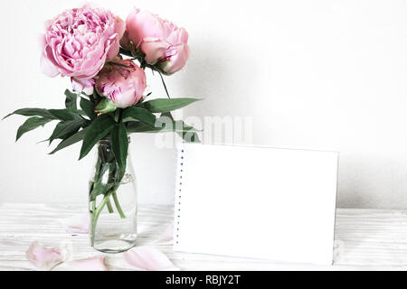 creative mock up with a beautiful bouquet of pink peony flowers and blankwhite greeting card with place for text. holiday or wedding background. low k Stock Photo